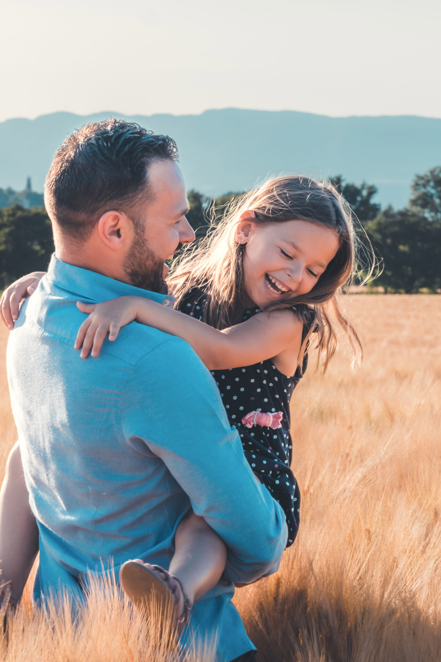 Papa qui soulève sa fille en riant dans un champ, séance photo famille Genève